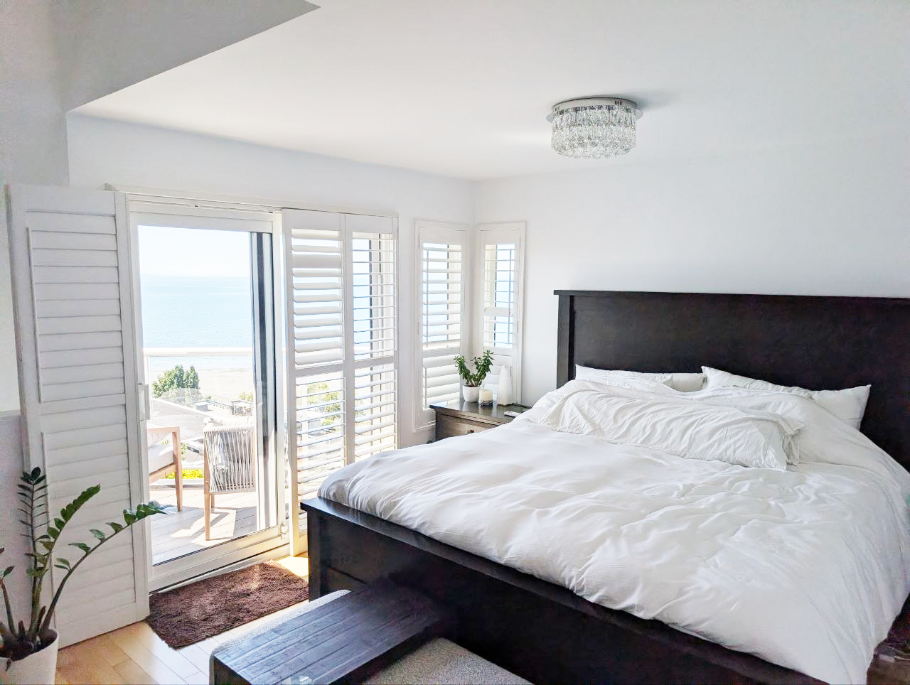 White Rock bedroom — dark wood bed frame with white linens and ocean view